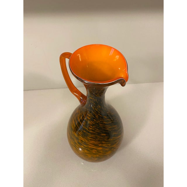 Very unusual pattern of a classic mid century cased glass pitcher. The handle is clear orange glass with the body of the...