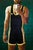 A figure in a black and gold athletic kit raises a phone overhead for a selfie, the body caught mid-gesture against a hum...