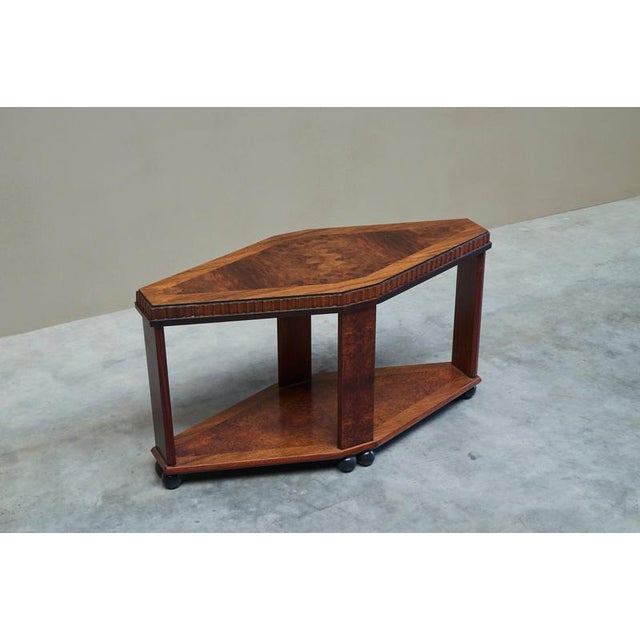 A stunning art deco side or center table in inlaid and mirrored burl veneer, carved edges and ebonized details. The table...