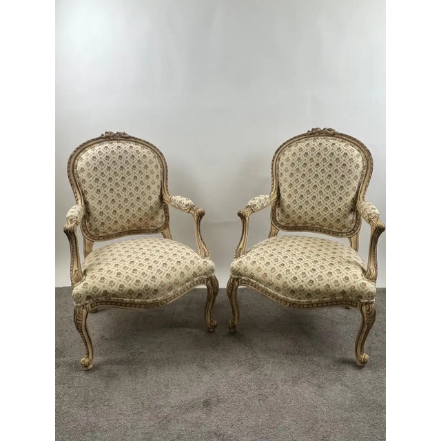 Pair of French Louis XV-style bergère armchairs, hand-carved with a soft cream and gilt-accented painted frame. Each chair...