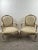 Pair of French Louis XV-style bergère armchairs, hand-carved with a soft cream and gilt-accented painted frame. Each chair...