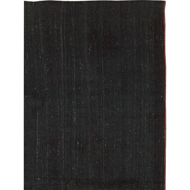 This Mid-20th century Turkish Flatweave Kilim rug, features a minimalist design centered around a deep, inky black field....