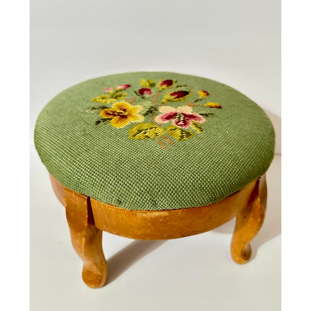 Vintage round wooden footstool with a sage green floral needlepoint top and short curved legs. The floral needlepoint is a...