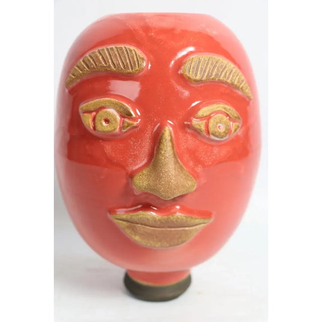 Studio pottery vase in the form of a persons head, orange ground glaze with gold scraffito facial features. Unsigned,...