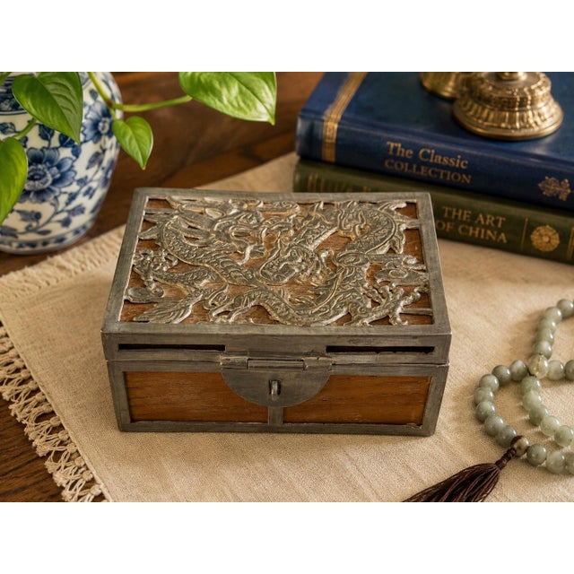 Vintage Chinese decorative box crafted with warm wood panels and an intricately detailed silver-tone dragon overlay. The...