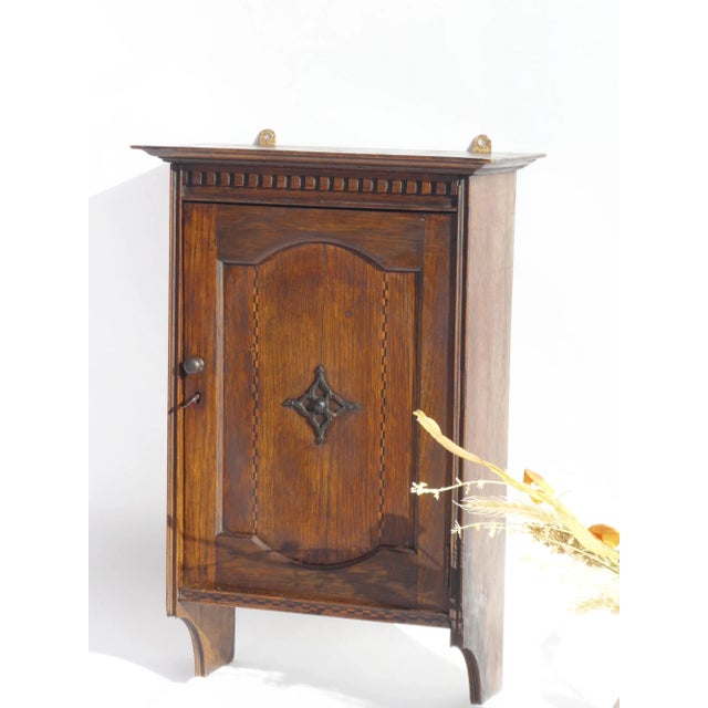 An antique dark wooden small cabinet with inlaid wood details on the front door. The apothecary has a beautiful ornament...