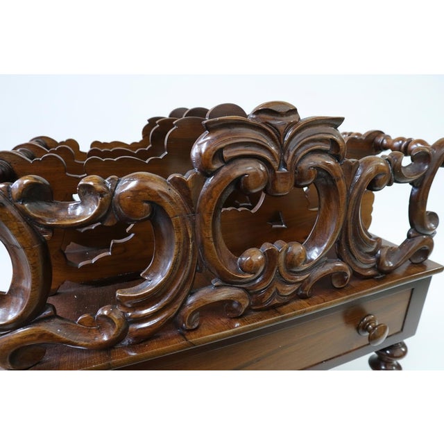 A finely carved raised mahogany Canterbury in the Rococo Revival taste, with turned spindles to the upper rails. The lower...