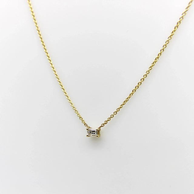 This 14k gold necklace features a beautiful emerald cut diamond, prong set in a rectangular setting, and suspended from a...