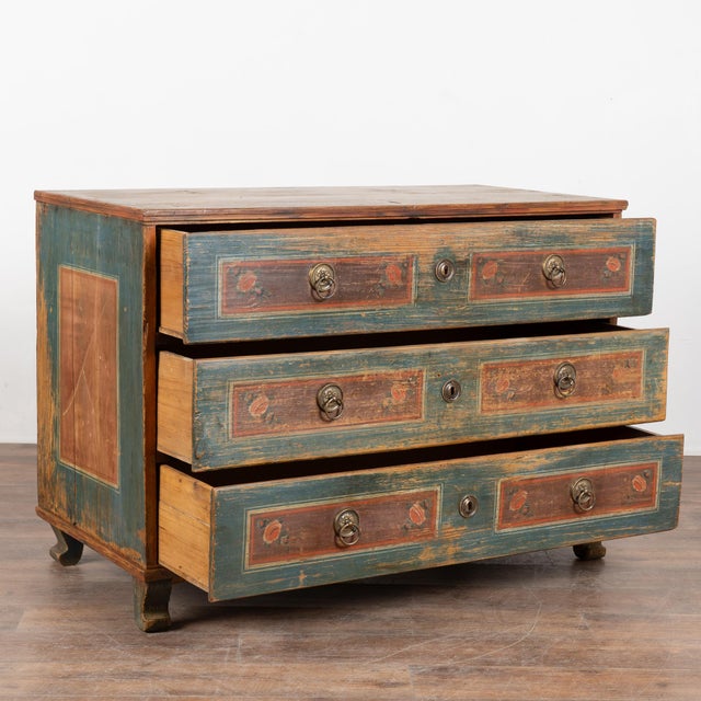 19th-century chest of three drawers crafted in pine with its original hand-painted finish. The background is a soft aged...