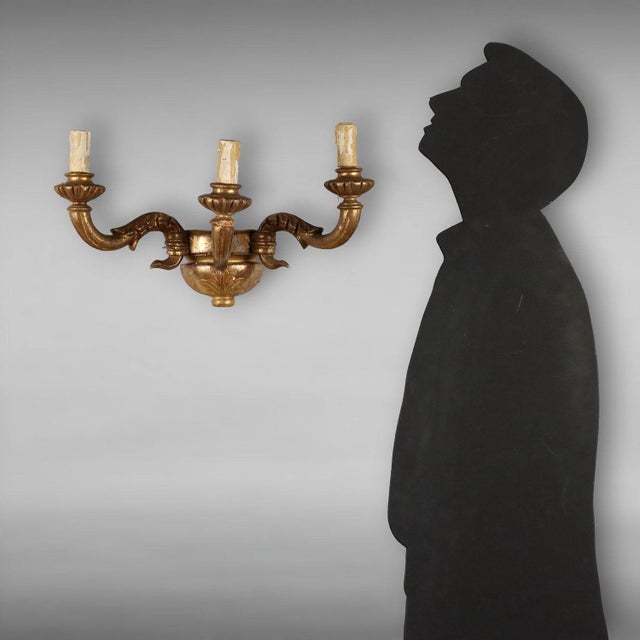 Three-light wall lamp in carved and gilded beech wood, wavy arms. Italy, early 20th century. This piece is attributed to...