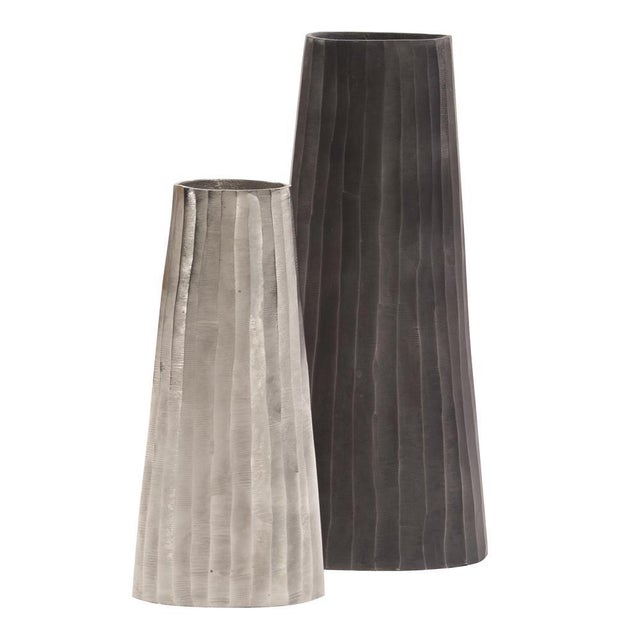 This metal vase features a tapered, triangular shape. It is characterized by a chiseled texture etched into the metal. It...