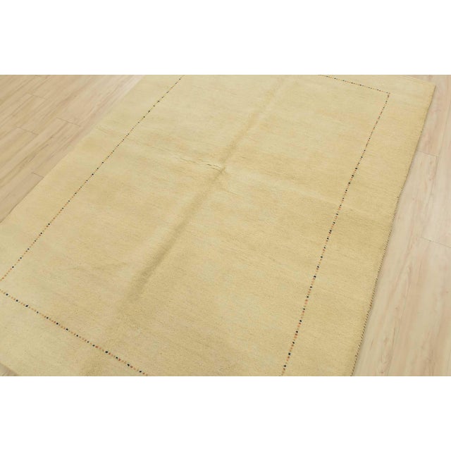 A contemporary Gabbeh rug hand-knotted with an all-wool pile on a cotton foundation. This area rug features a solid ivory...