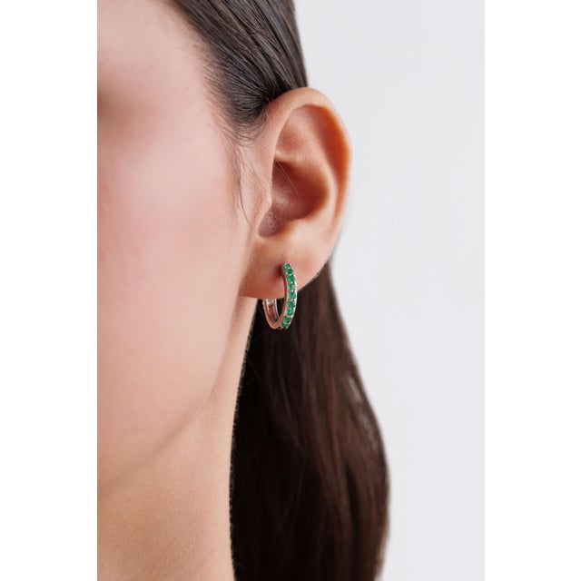 These elegant huggie hoop earrings feature a 0.67 ct row of vivid green emeralds and diamonds, set in 18k white gold. Each...