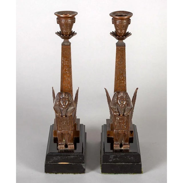 Pair bronze Egyptian Revival candlesticks with winged Sphinx sitting before an obelisk inscribed with hieroglyphics,...