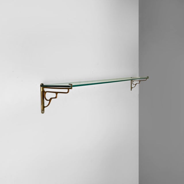 Italian Art Deco shelf in glass and brass, 1930s Rectangular glass wall shelf. The struts are in curved brass rods. Art...