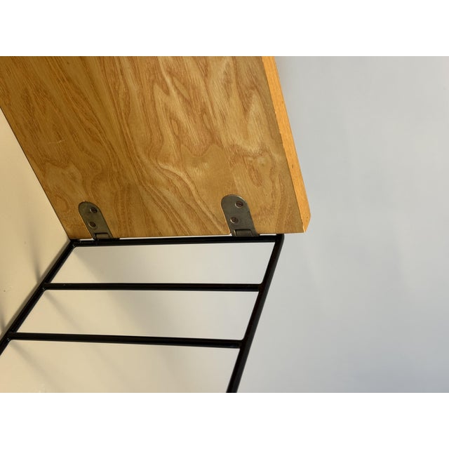 This wall-mounted shelving unit from the 1960s features three wooden shelves combined with black metal side supports. The...