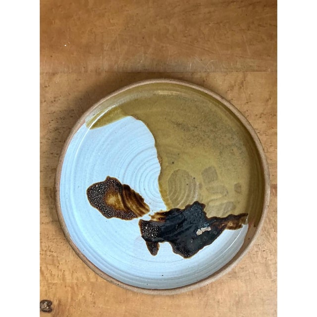 This vintage stoneware plate presents a bold, abstract glaze composition, with a creamy, unglazed white body serving as...