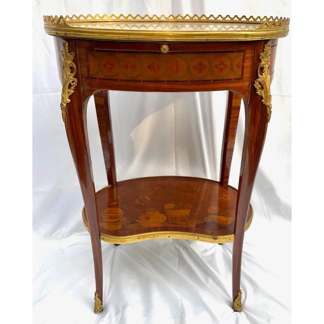 Elegant French Transitional Louis XV/XVI oval marquetry side table, adorned with ormolu mounts and a decorative gallery....