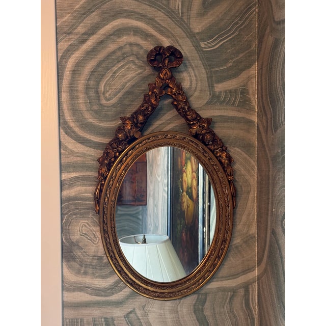 Louis XV style giltwood oval mirror, the frame carved with running ribbon and beaded borders, surmounted by a crossed...