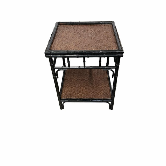 Vintage black two tier bamboo two tier table. A wood underlay supports a brown woven rattan herringbone pattern on the top...