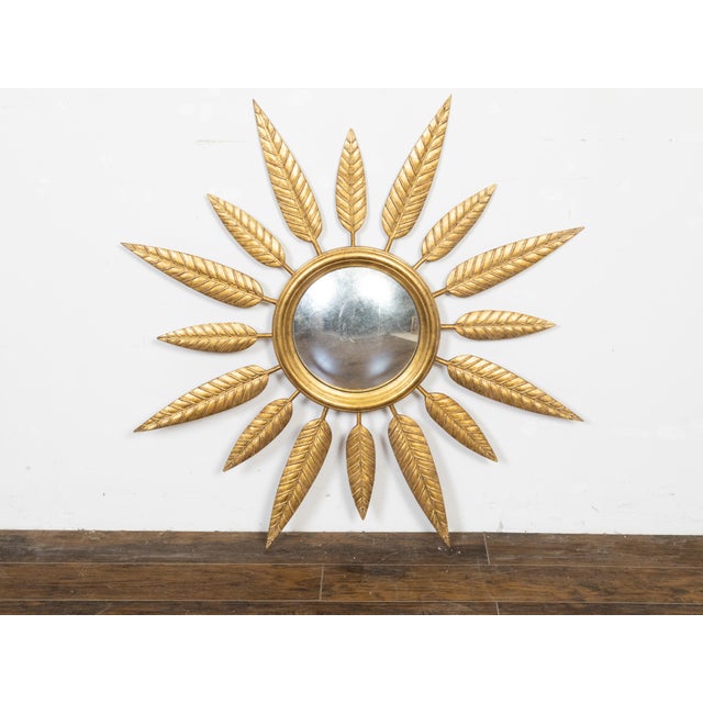 A vintage French gilt metal sunburst mirror from the mid 20th century, with convex plate, foliage leaves and molded frame....