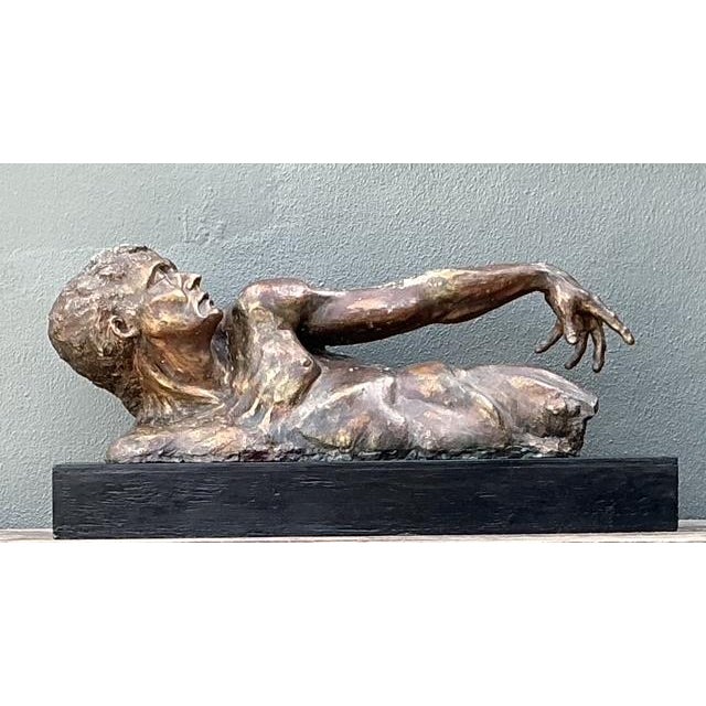 This substantial figurative sculpture captures a moment of intense physical exertion, depicting a recumbent male form...