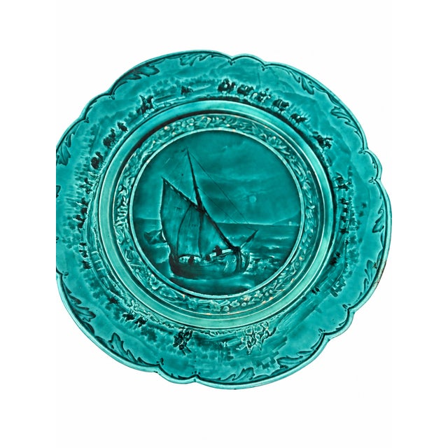 Five turquoise-green faïence plates with scalloped rims, richly patterned borders, and distinct pictorial centers...