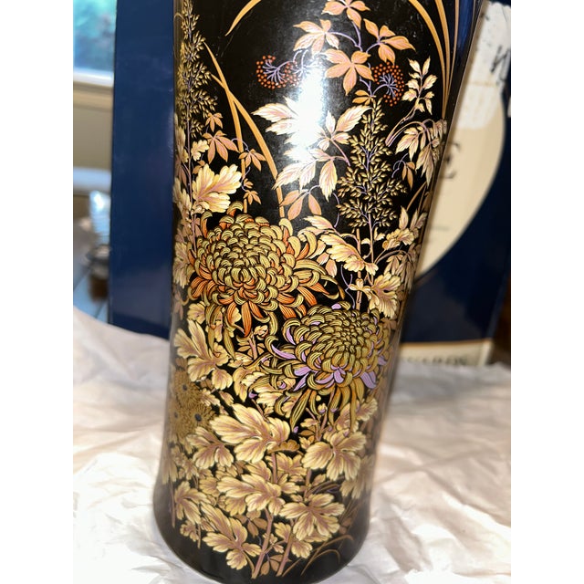 Elegant black decorative vase featuring intricate gold floral motifs. Subtle touches of purple and warm tan tones enhance...