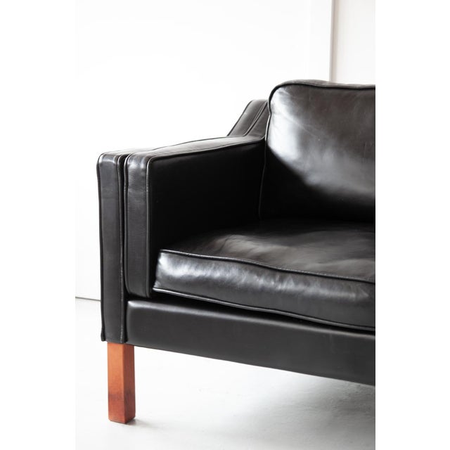 A Danish two-seater sofa in black leather with beech legs, designed in the style of Børge Mogensen. This compact sofa is...