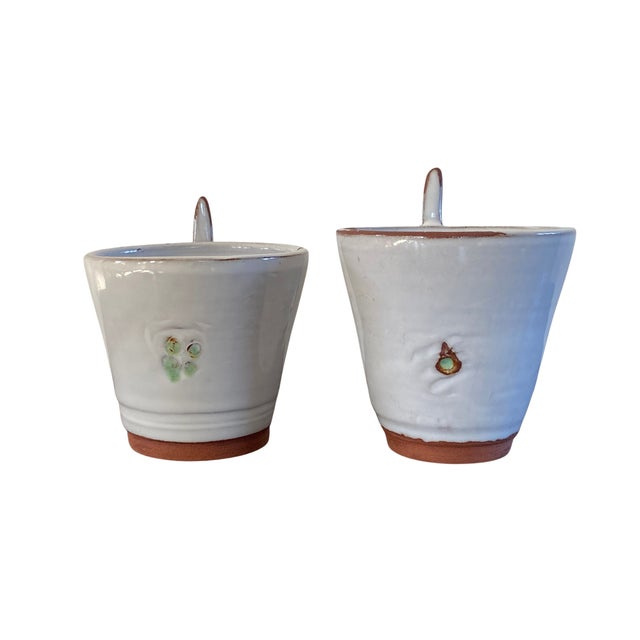 A distinctive pair of handcrafted studio pottery espresso cups featuring sculptural thumbhole handles and a soft, satin...