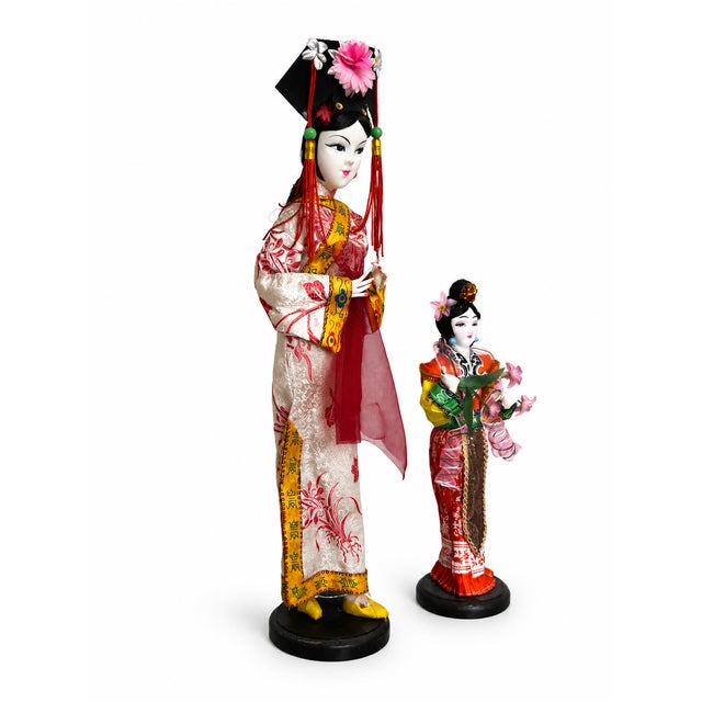 A striking pair of vintage Chinese costume display dolls, presented in contrasting heights on individual black round...