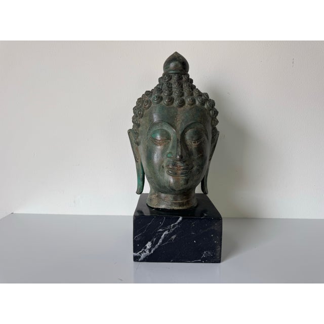 Striking vintage bronze Buddha head sculpture featuring a beautifully aged verdigris patina and mounted on a solid black...