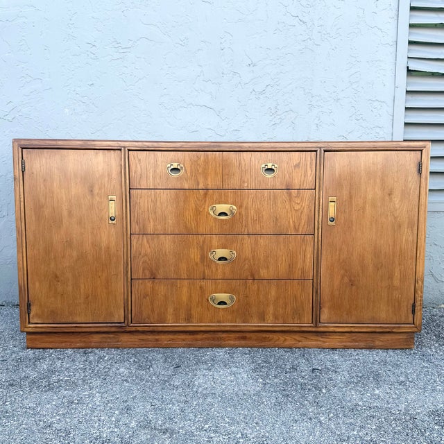 This vintage campaign credenza by Drexel pairs warm, richly grained wood with classic recessed brass hardware. Four...