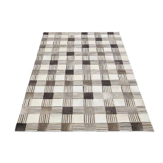 A contemporary leather and wool rug with a geometric patch design with beige, gray, and brown accents, made with 100%...