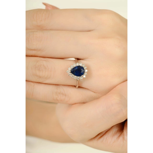 This engagement ring features a 1.62-carat royal blue pear cut sapphire at its center, surrounded by a halo of round...