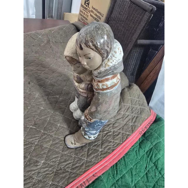 A charming vintage Lladró porcelain figurine depicting two children in winter dress sharing a tender embrace. This...