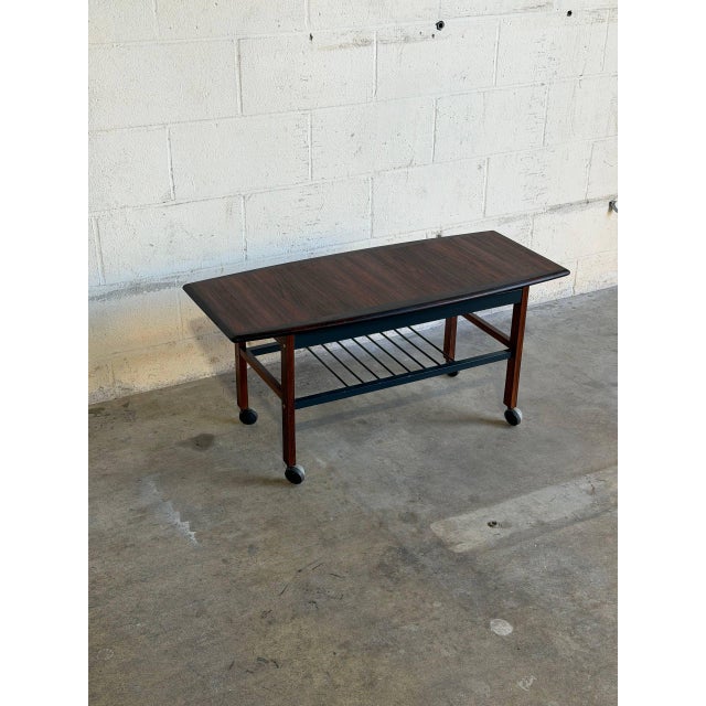 This sleek Danish-inspired coffee table trolley blends mid-century sophistication with everyday mobility. It features a...