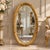 Elegant Italian style vertical oval wall mirror featuring an ornate gold leaf frame beautifully enhanced with decorative...