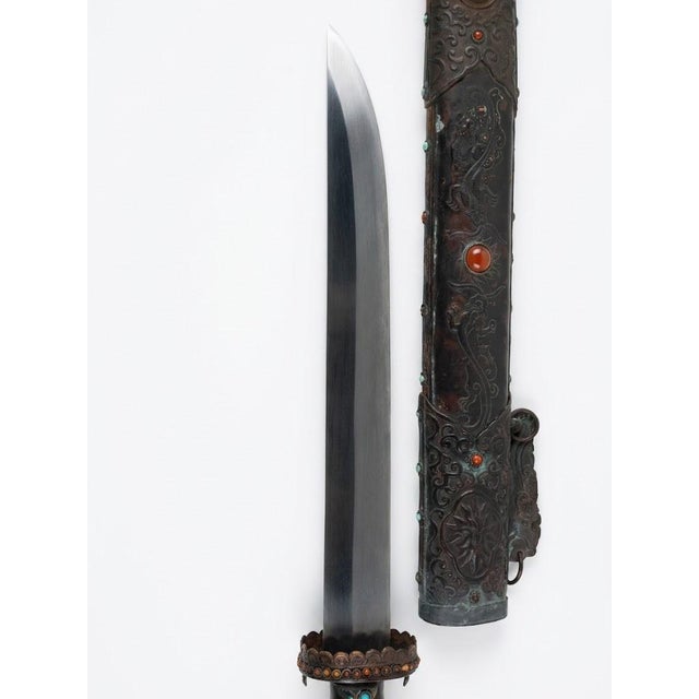 This is a decorative knife with a carved wooden sheath featuring floral and scroll designs accented by colored stones. The...