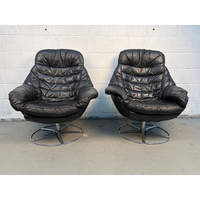 Sleek and comfortable pair of lounge chairs upholstered in smooth black leather. Featuring a swivel base and clean, modern...