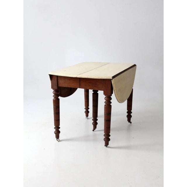 An antique drop-leaf dining table with a classic turned-leg silhouette and beautifully aged character. The wooden table...