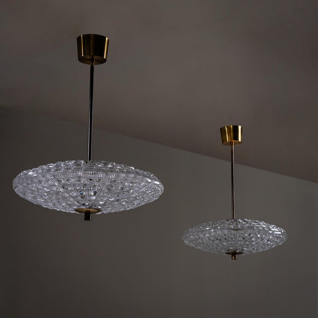Pair of pendant lights with elongated brass stems and wall mounts, featuring lens-shaped bodies in pressed crystal glass....