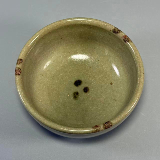 This compact‑sized celadon bowl features soft olive‑green glaze with natural speckled markings. The piece has a neatly...
