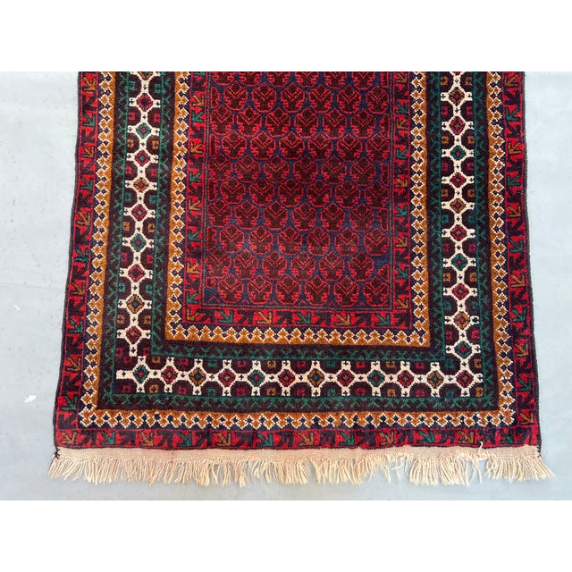 A vintage Afghan Baluch wide runner carrying an all-over boteh (paisley) lattice across a deep oxblood field, framed by...