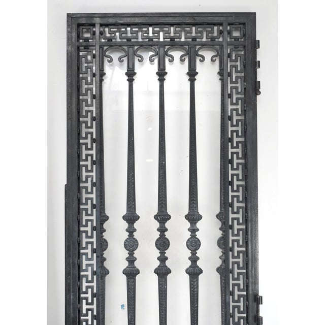 French style entry double doors made of wrought iron with a Greek key frame design and an ornate relief panel. The...