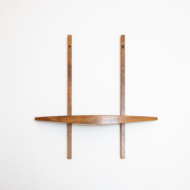 A sculptural solid wood wall shelf with a gently arched front and tapered profile that becomes thinner toward each end....