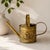 Decorative vintage brass watering can featuring richly embossed roses and foliage throughout the cylindrical body....