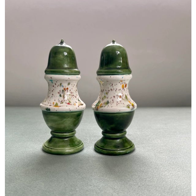 A pair of salt and pepper shakers in a colonial revival shape with a green foot and top and a rainbow speckled white glaze...