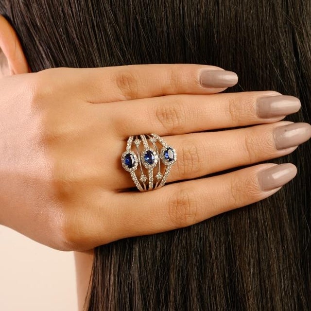 This elegant ring is crafted in 14K white gold, showcasing a 1-carat oval-cut blue sapphire as the centerpiece. The...