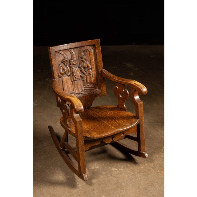 Antique quarter-sawn oak rocker with a carved panel splat. This unique piece depicts a scene wherein two monks appear to...